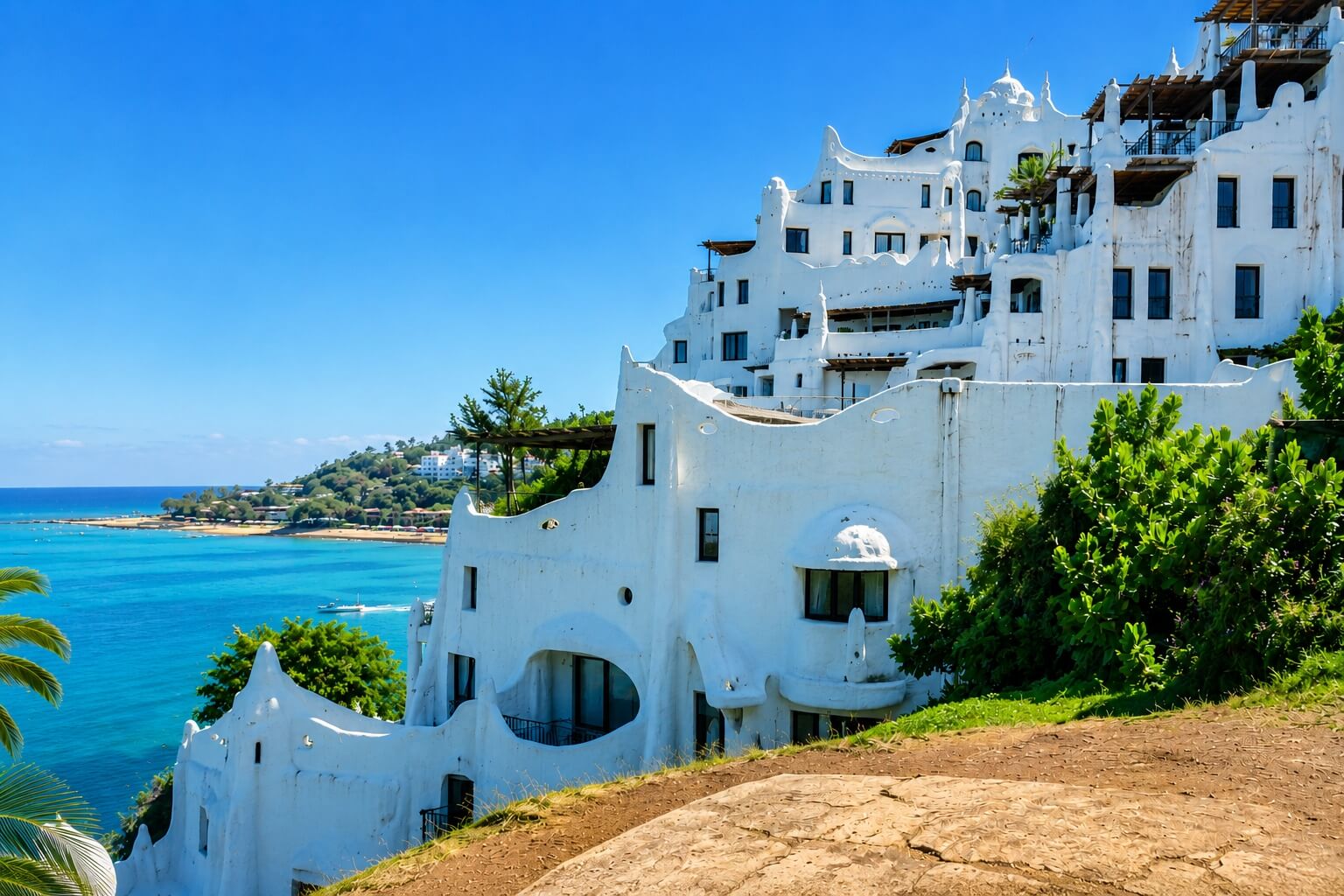 Vista panorâmica da Casa Pueblo em Punta del Este, Uruguai, com arquitetura branca icônica à beira-mar e céu azul em dia ensolarado.