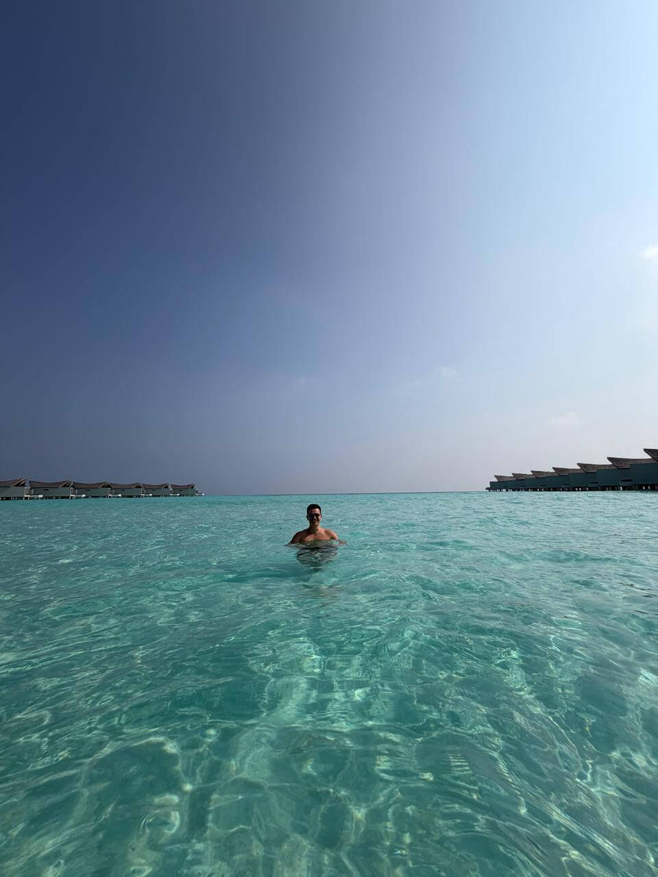 Homem na escada de acesso ao mar direto do deck da vila sobre as águas do Kuredhivaru Resort, Maldivas, com lagoa cristalina e vilas ao fundo