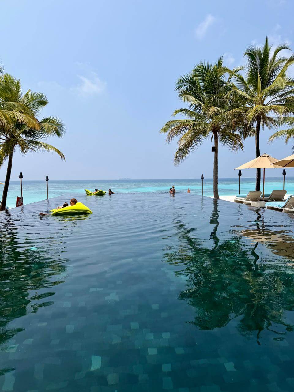 Piscina infinita do Kuredhivaru Resort nas Maldivas com coqueiros, espreguiçadeiras e vista para o oceano