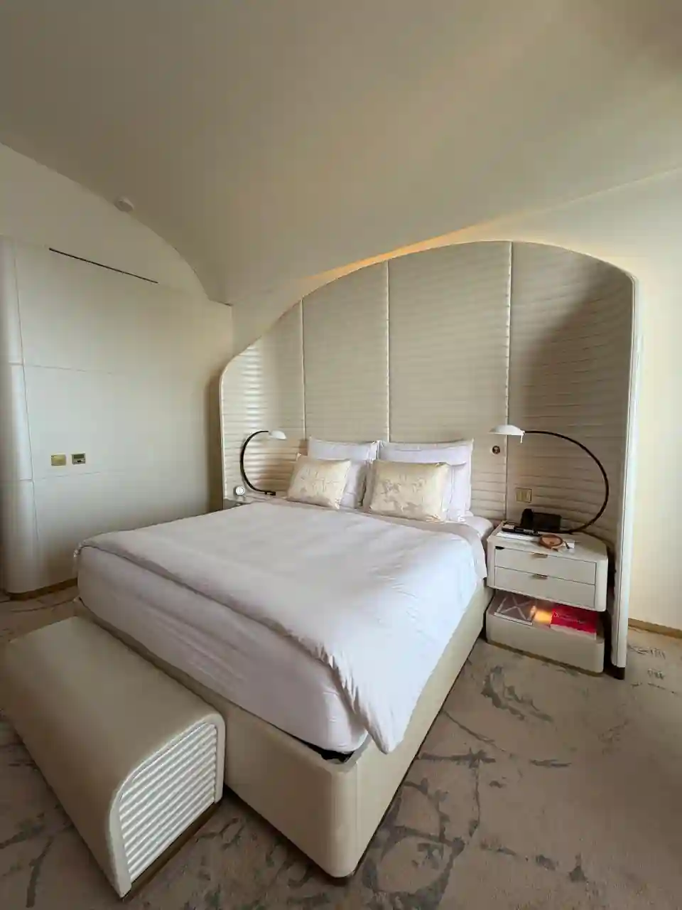 Cama do quarto do Fairmont Doha, com cabeceira arredondada e iluminação ambiente