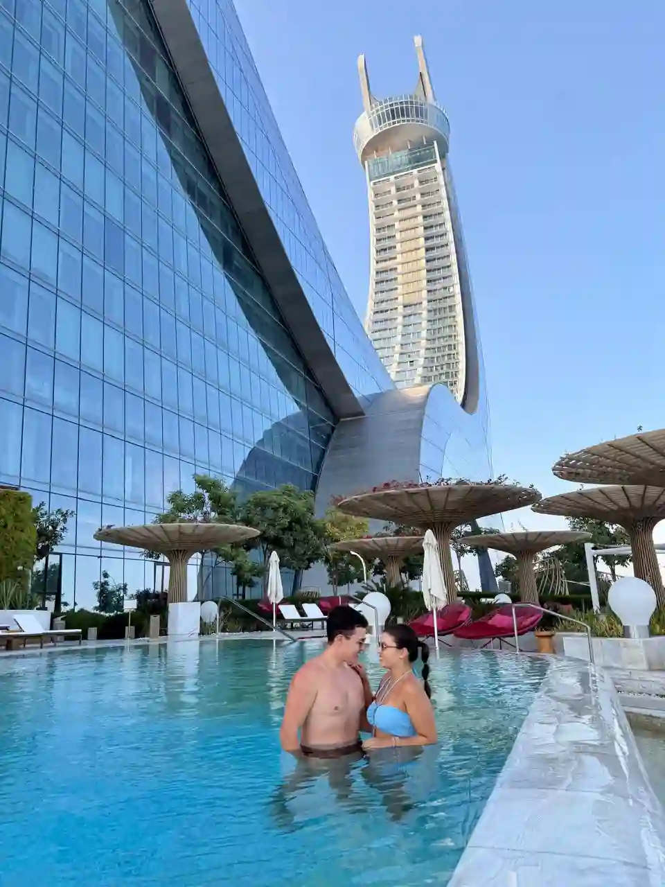 Casal na piscina do Fairmont Doha com as Katara Towers ao fundo
