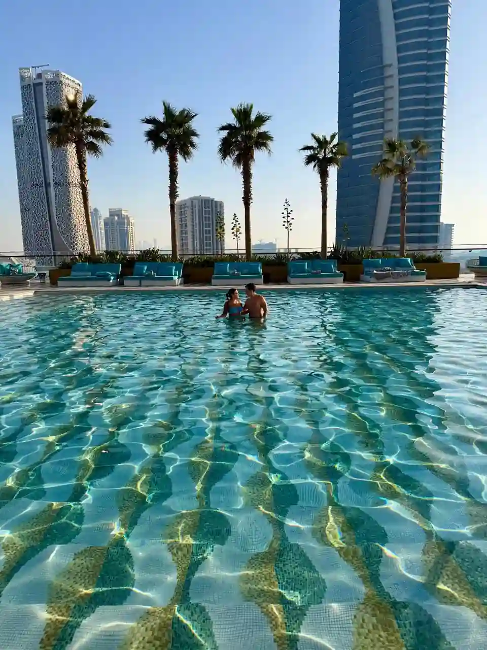 Casal na piscina do Fairmont Doha com vista da skyline de Lusail