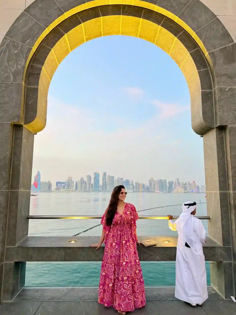 Mulher em arco dourado do Museu de Arte Islâmica com vista da skyline de Doha ao fundo