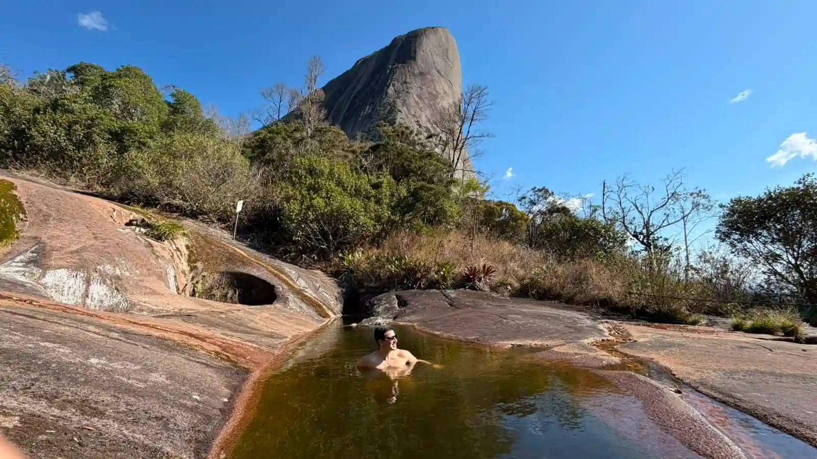 Homem nadando em piscina natural com a Pedra Azul ao fundo