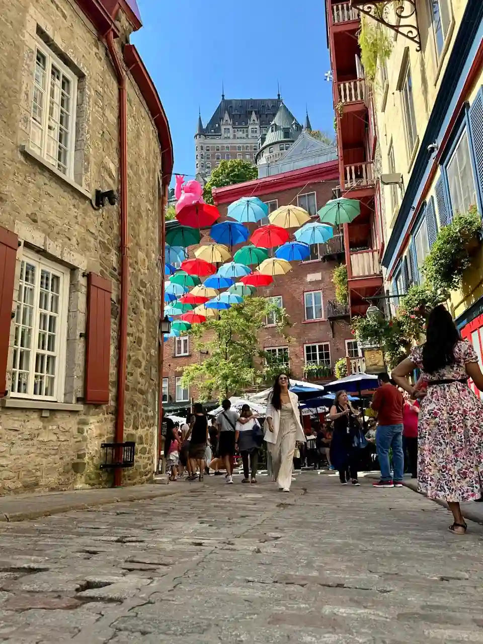 Rua com guarda-chuvas coloridos no Quartier Petit-Champlain, com o Château Frontenac ao fundo