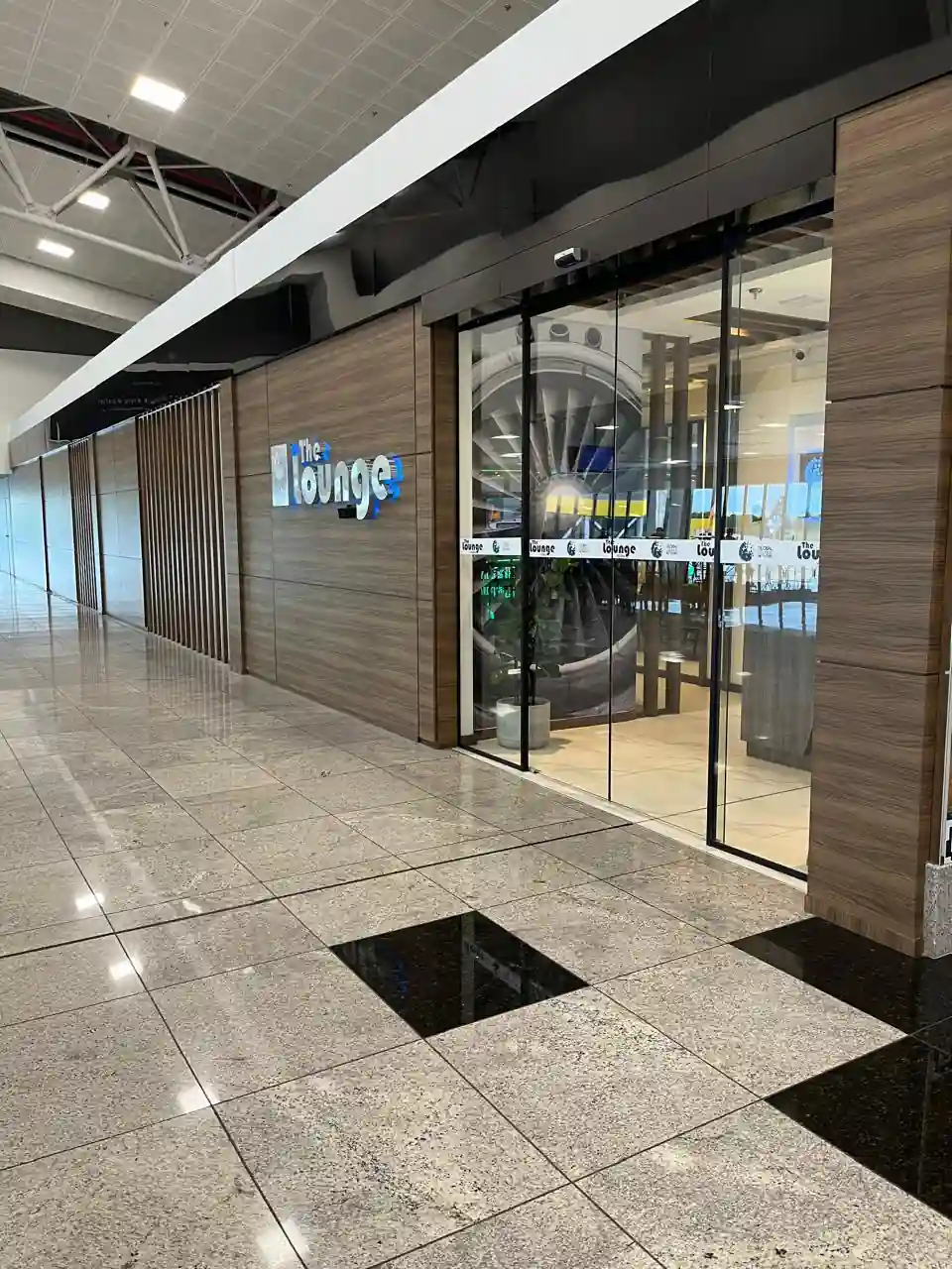 Entrada da Sala VIP The Lounge no Aeroporto de Vitória (VIX), com letreiro iluminado e porta de vidro
