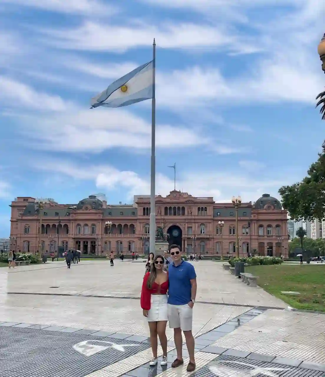 Casal em frente à Casa Rosada, com a bandeira da Argentina, em Buenos Aires